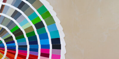 Ein bunter Farbfächer ragt von links ins Bild. Der Hintergrund ist grau.