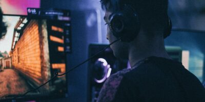 Ein junger Mann sitzt mit Kopfhörern vor einem Computerbildschirm. Der Bildschirm zeigt die Mauer eines alten Hauses.